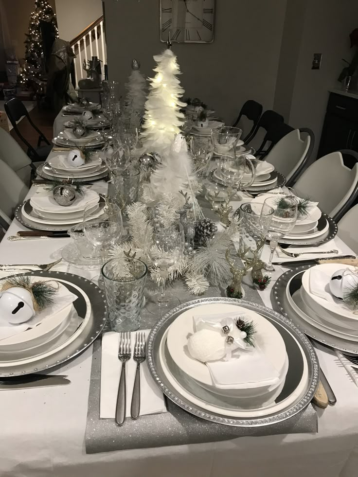 the table is set with silver and white plates, silver napkins, pine cone centerpieces