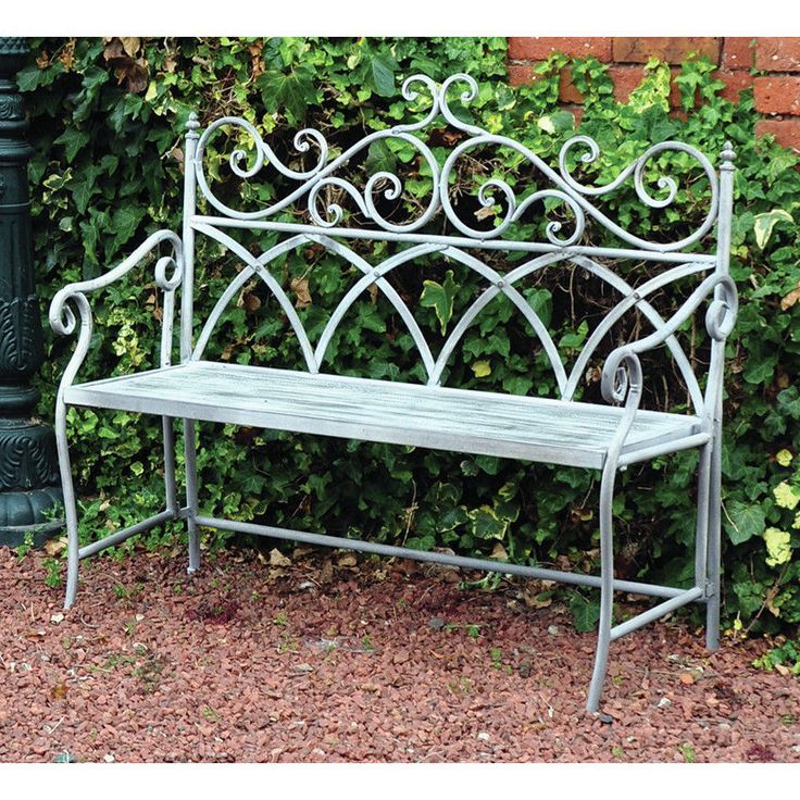 a metal bench sitting next to a green bush