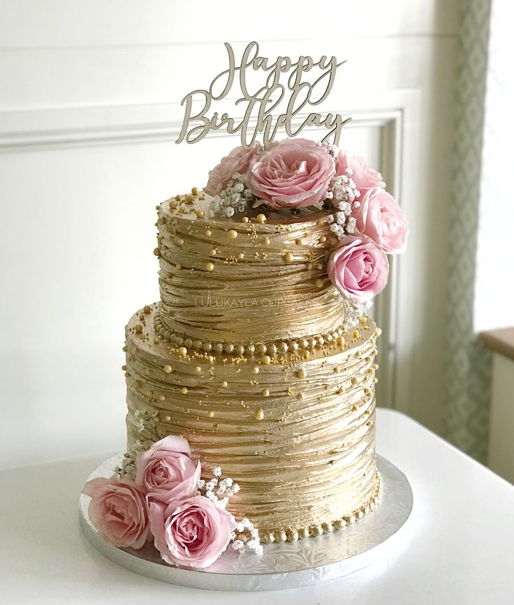 a three tiered cake with pink flowers on top and a happy birthday sign in the middle