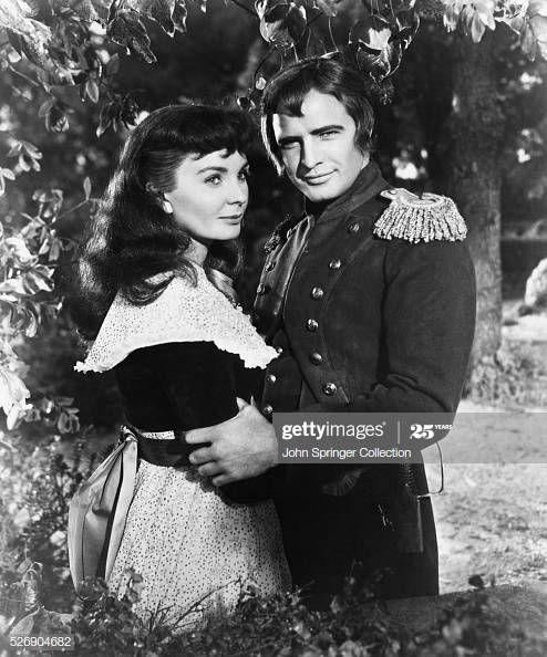 an old black and white photo of two people standing next to each other under a tree