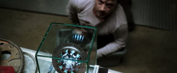 a man is looking down at a clock in a glass case on a table next to other items