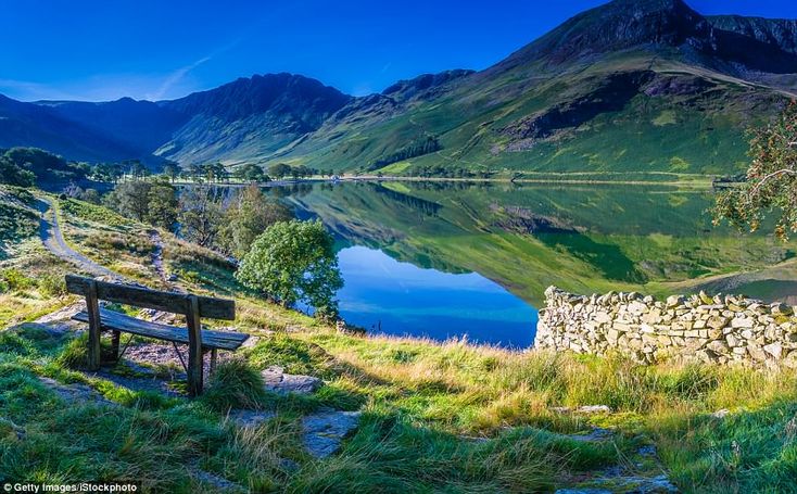 a bench sitting on top of a grass covered hillside next to a lake with mountains in the background