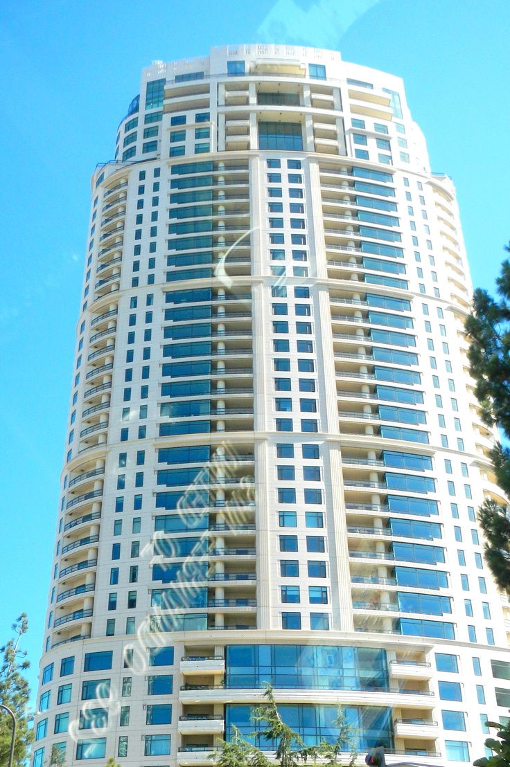 a tall white building sitting next to a lush green tree filled park on a sunny day