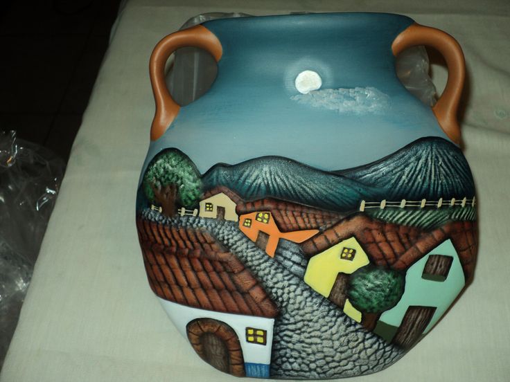 a ceramic vase painted with houses and mountains in the background, sitting on a table