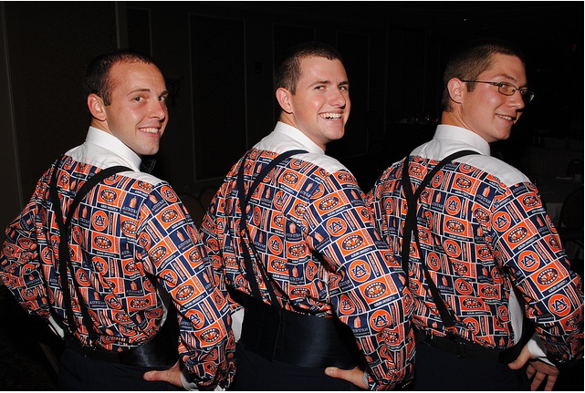 three men in patterned shirts and suspenders smile at the camera