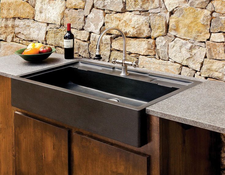 a kitchen sink sitting next to a counter top under a bottle of wine and bowl of fruit