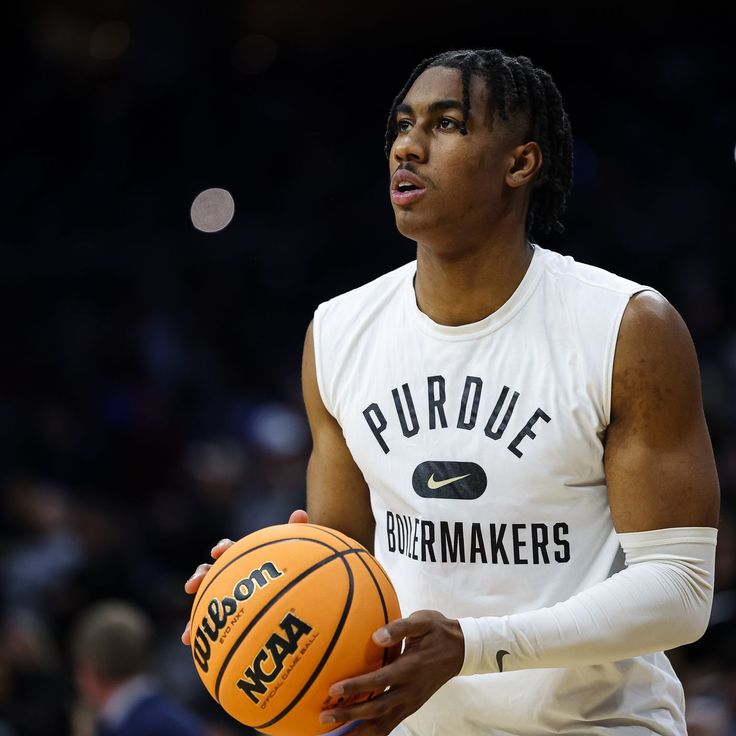 a man holding a basketball in his right hand and wearing a white shirt with the word purdue on it