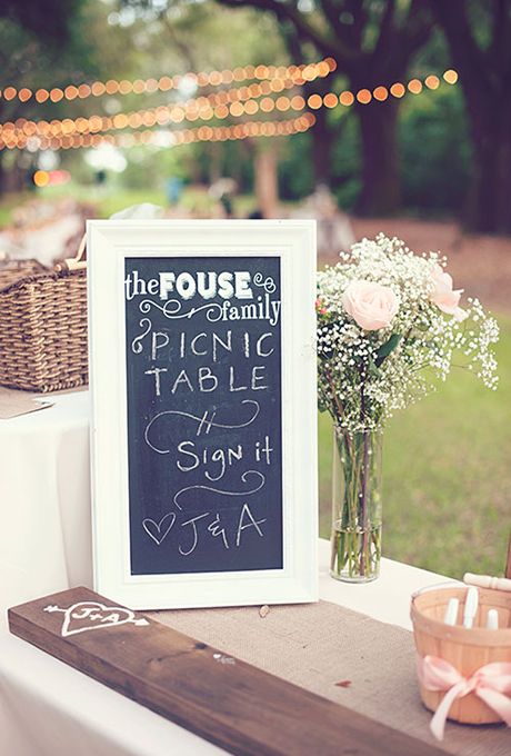 a wooden table topped with a vase filled with flowers and a chalkboard sign on top of it