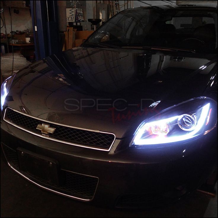 the front end of a black chevrolet camaro in a garage with its lights on