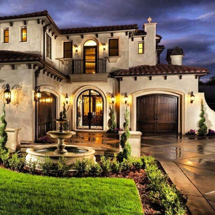 a large house with a fountain in the front yard and landscaping around it at night