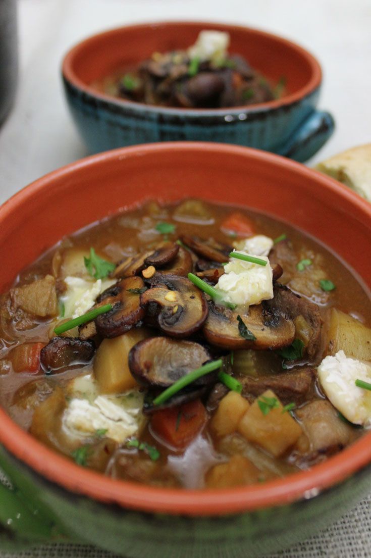 two bowls filled with soup and vegetables on top of a white tablecloth next to bread