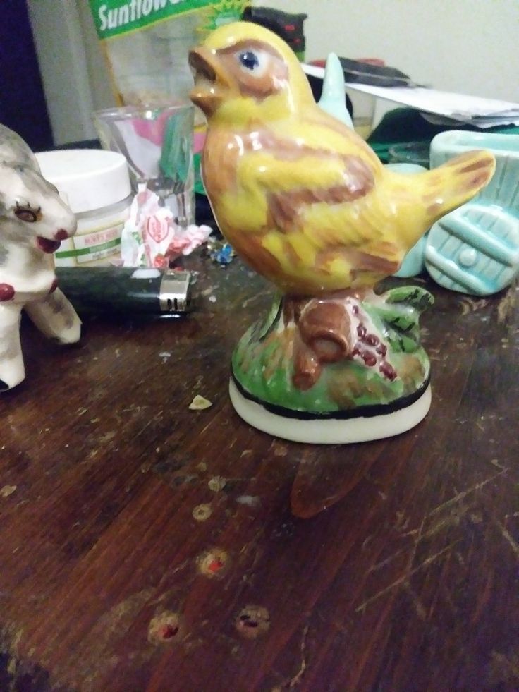 a ceramic bird sitting on top of a wooden table next to a white dog and other items