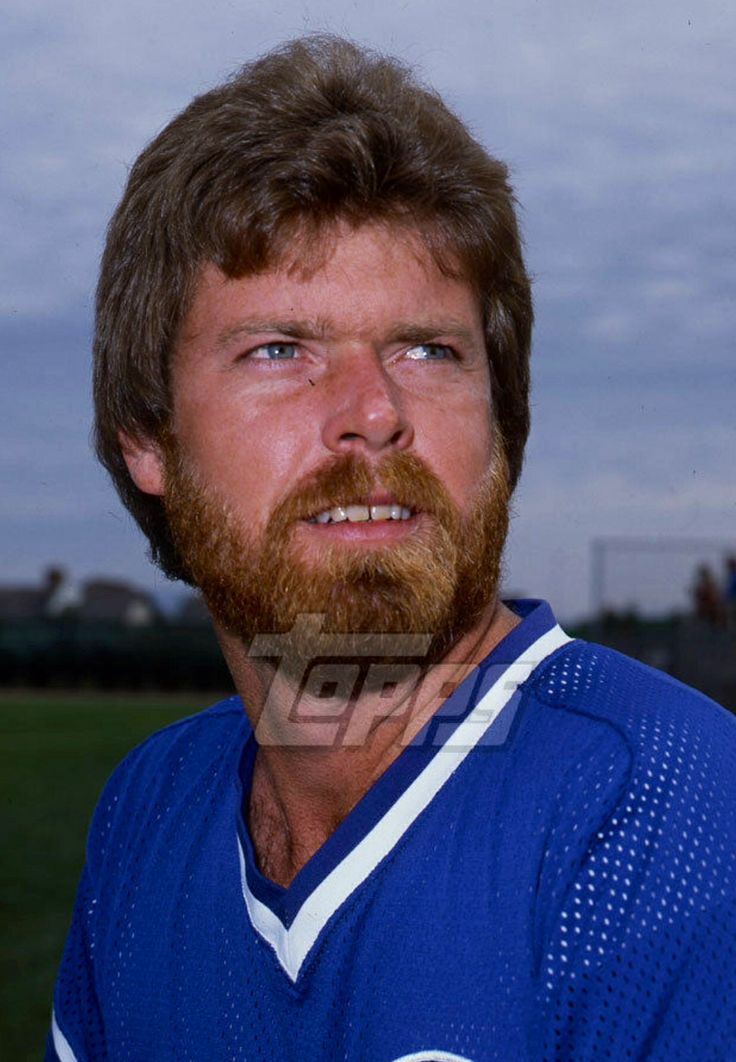 a close up of a baseball player with a beard wearing a blue uniform and looking at the camera