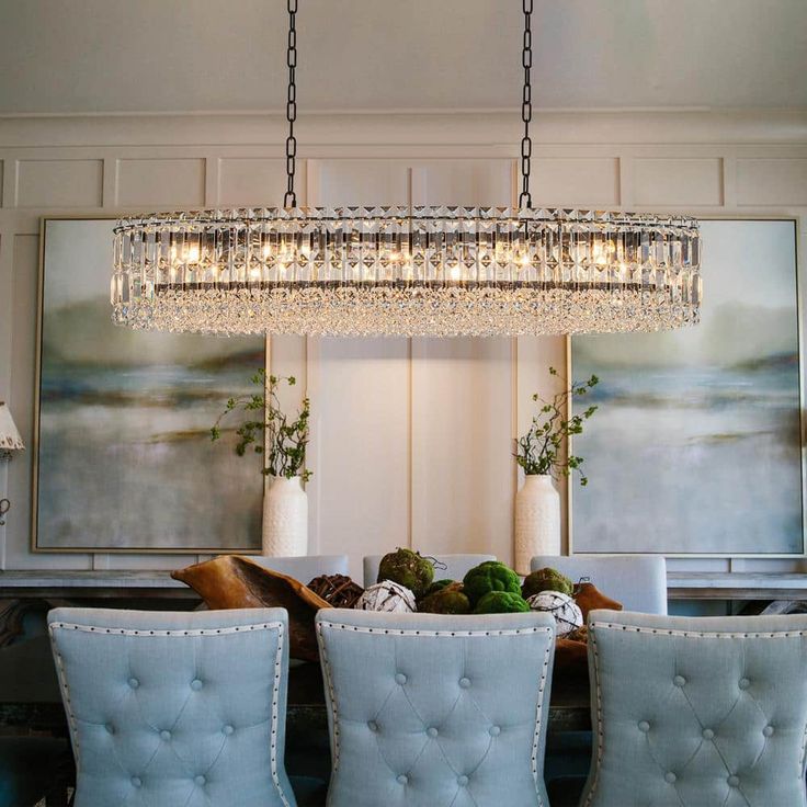 a chandelier hanging over a dining room table with four chairs and a vase filled with flowers