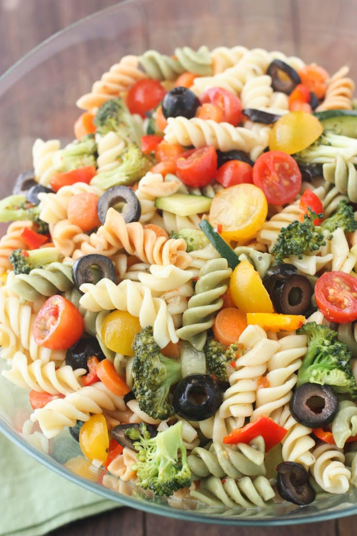 a pasta salad with tomatoes, broccoli and olives in a glass bowl