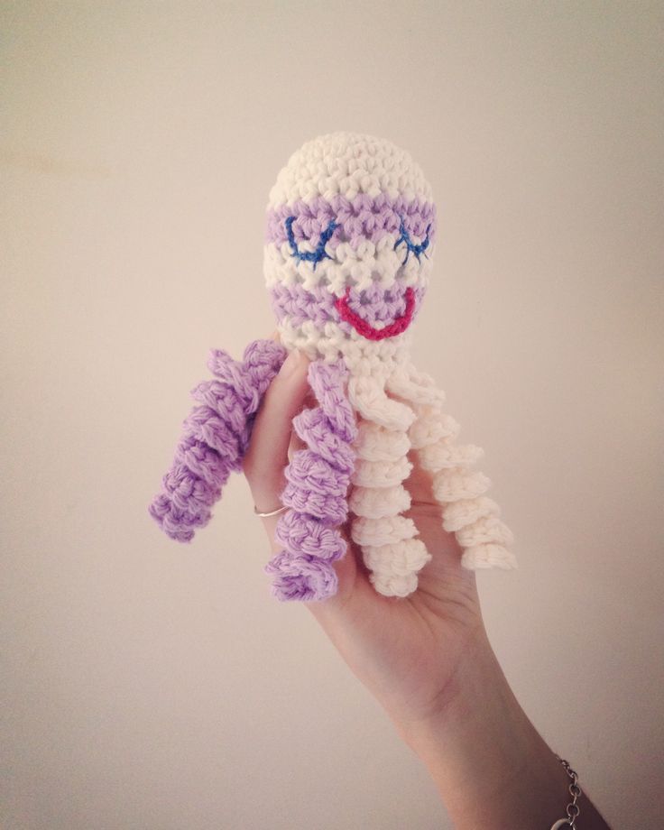 a hand holding a crocheted purple and white doll with blue eyes, smiling