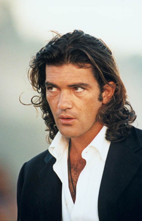 a man with long hair wearing a black suit and white shirt looking off to the side