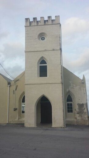 an old church building with a clock on it's front and side windows, in the middle of a parking lot