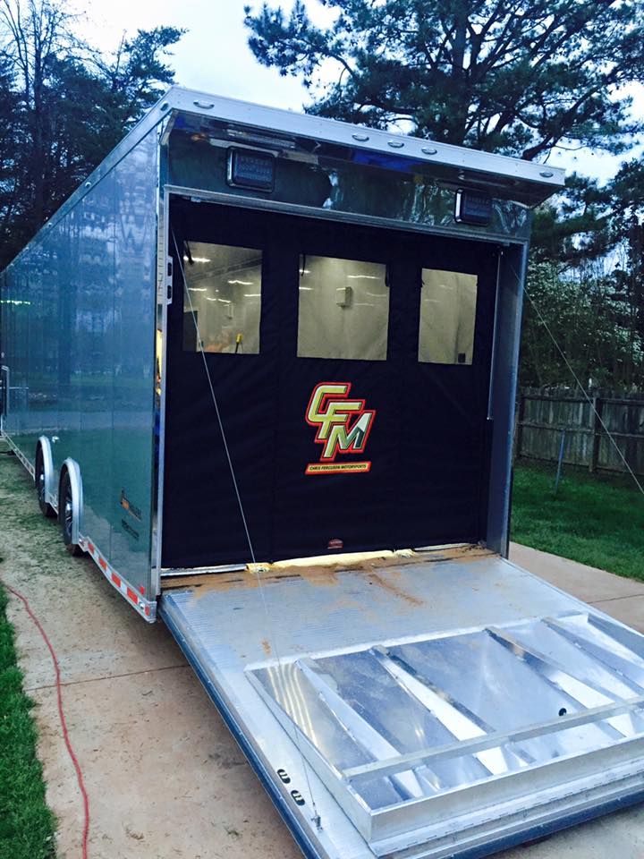 an enclosed trailer with the door open on a sidewalk in front of some trees and grass