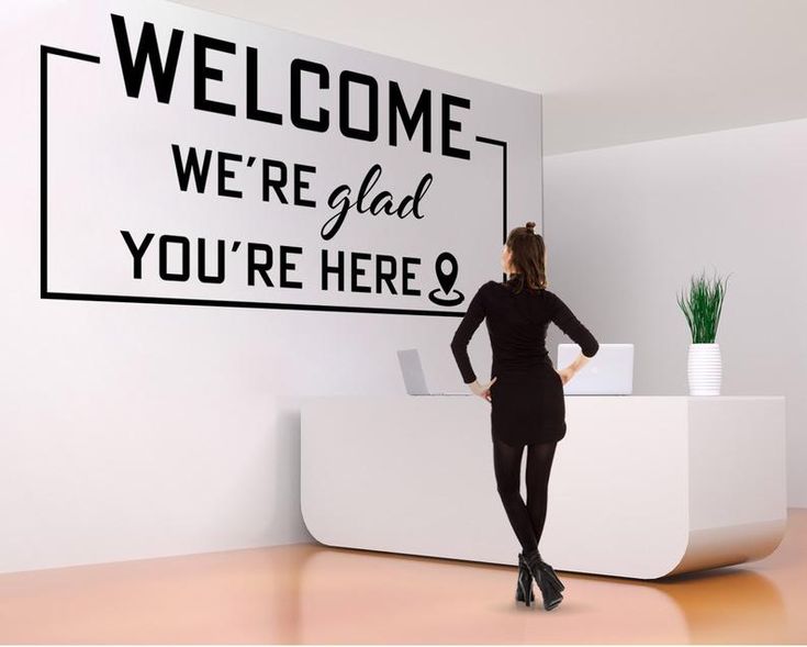 a woman standing in front of a welcome sign with the words we're glad you're here