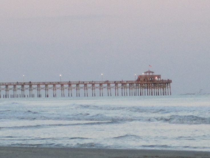 a long pier on the beach with waves coming in