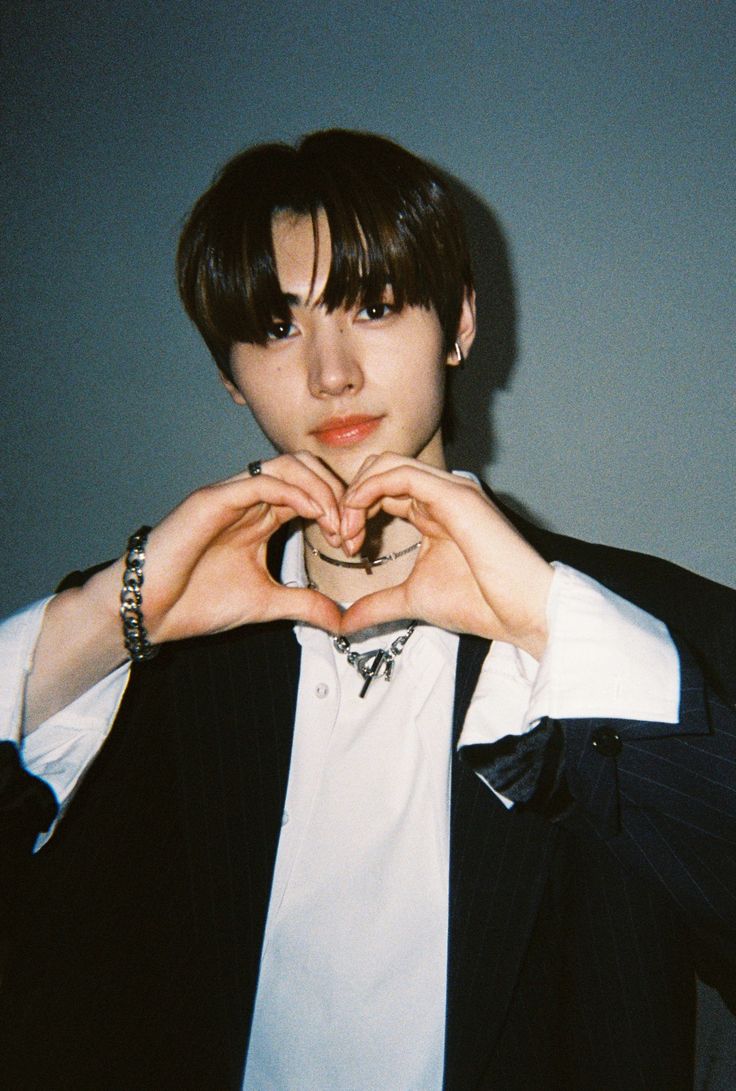 a young man making a heart with his hands while wearing a black and white suit