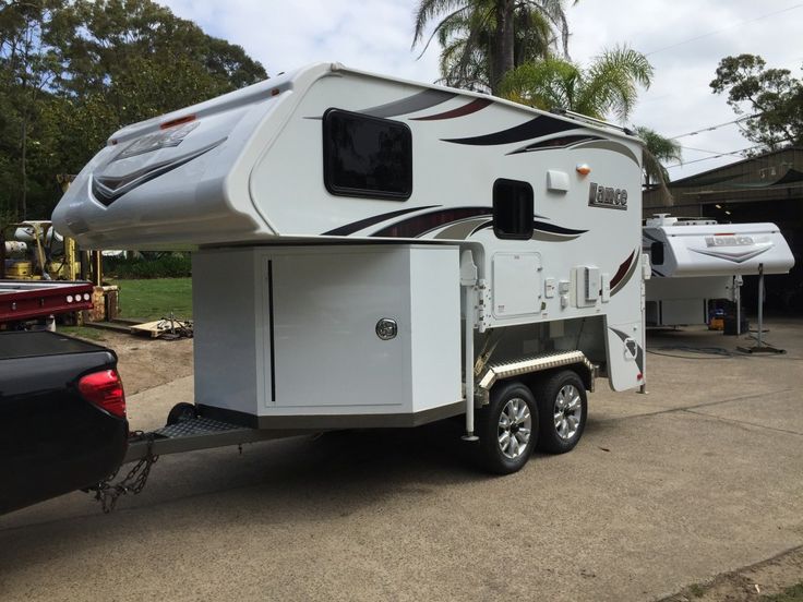 an rv parked in front of a trailer on the side of a road next to some trees