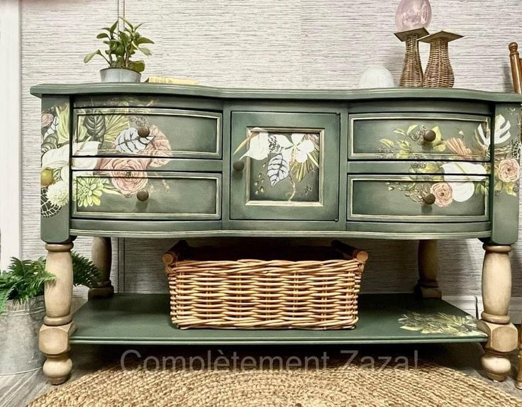 a green dresser with flowers painted on the drawers and wicker basket under it, next to potted plants