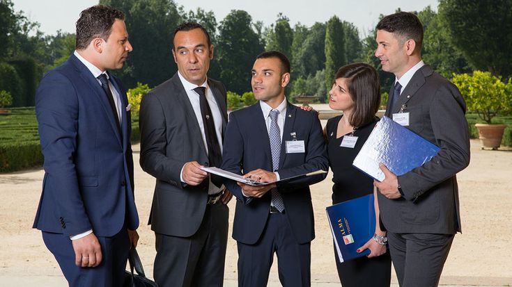 three men and two women in business attire talking to each other while holding folders