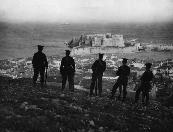 several men standing on top of a hill looking out at the ocean and town below