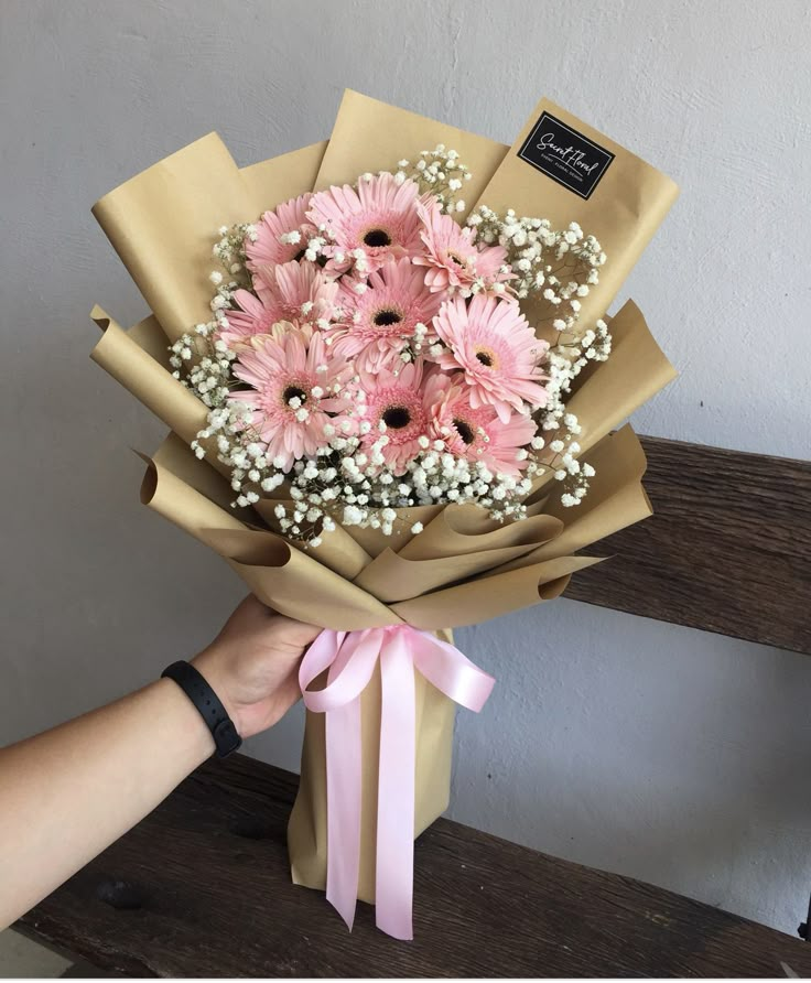 a person holding a bouquet of pink flowers on a wooden bench in front of a wall