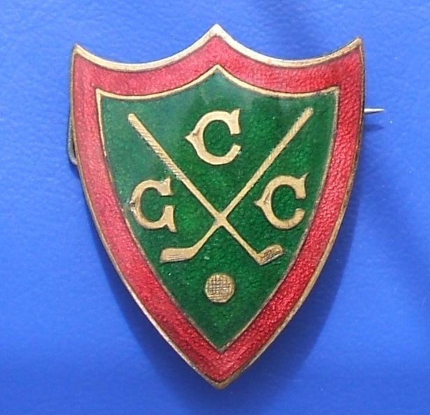 a green and red shield with two crossed golf clubs on it's side against a blue background