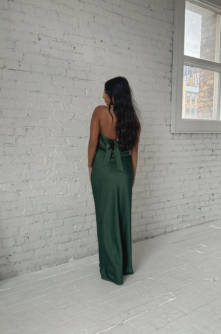 a woman standing in front of a brick wall wearing a green dress with a bow at the back