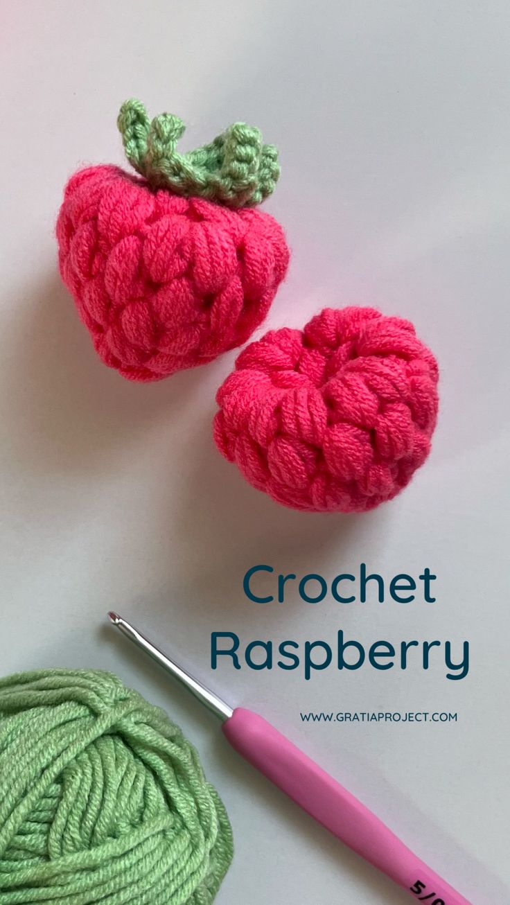 two crochet raspberries next to a ball of yarn and a knitting needle