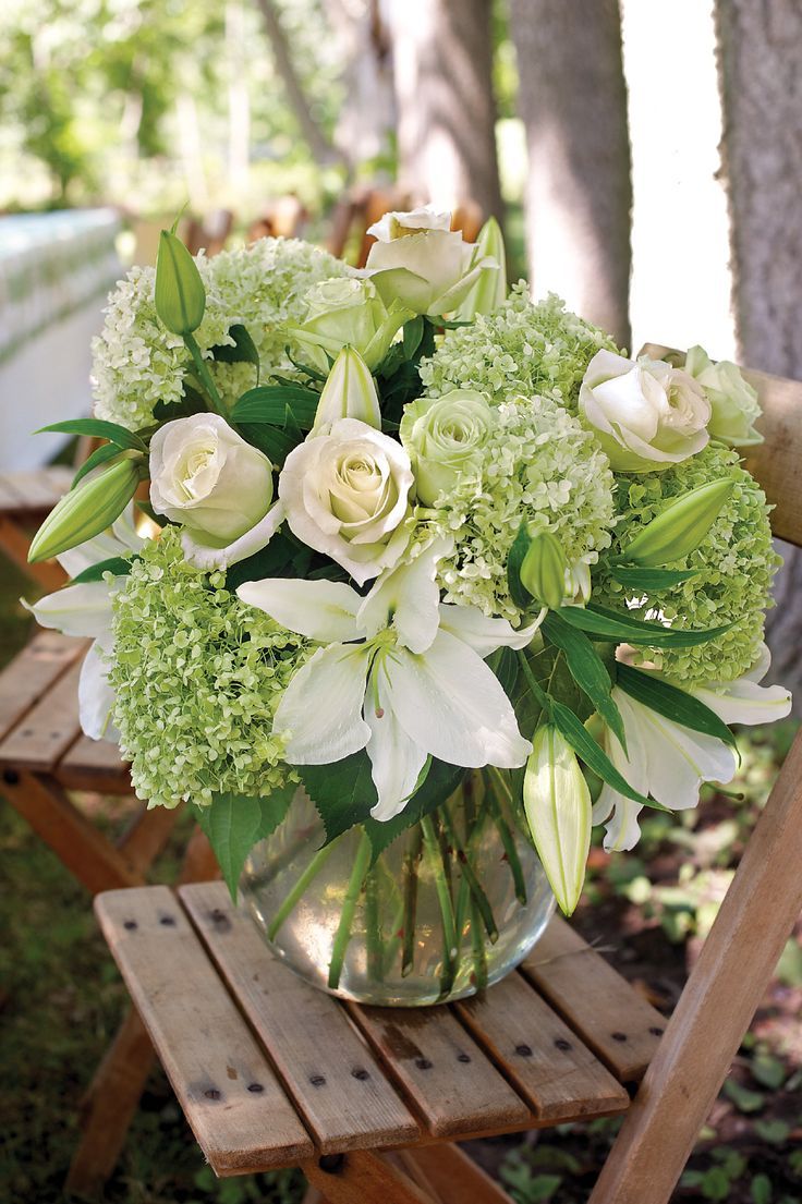 a vase filled with white and green flowers on top of a wooden chair next to a tree