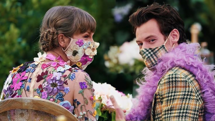 a man and woman wearing face masks standing next to each other in front of flowers