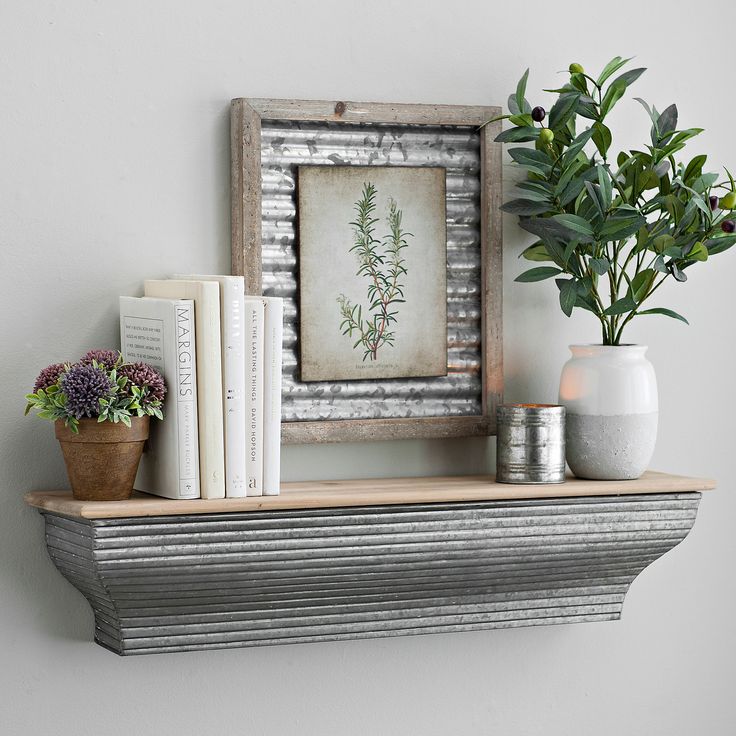 a shelf with some books and plants on it next to a wall mounted picture frame