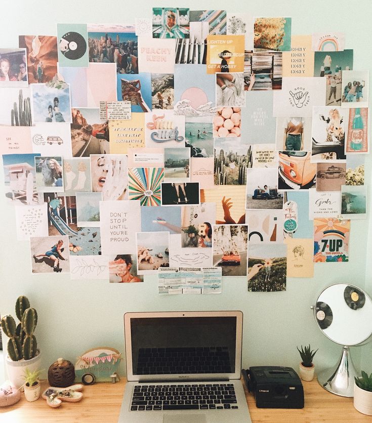 a laptop computer sitting on top of a wooden desk next to a wall covered in pictures