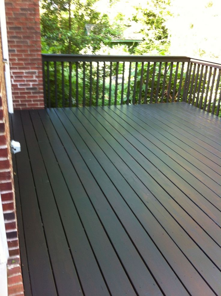 a wooden deck with railings and trees in the backgroung area, next to a brick building