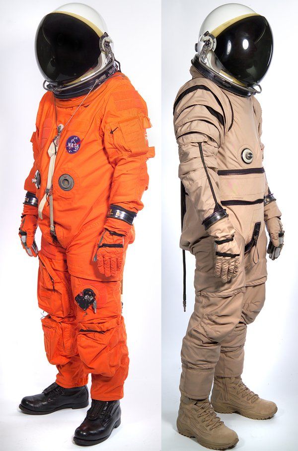 two men in spacesuits standing side by side, one wearing an orange space suit