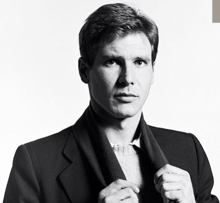 a black and white photo of a man in a suit holding his tie over his shoulder