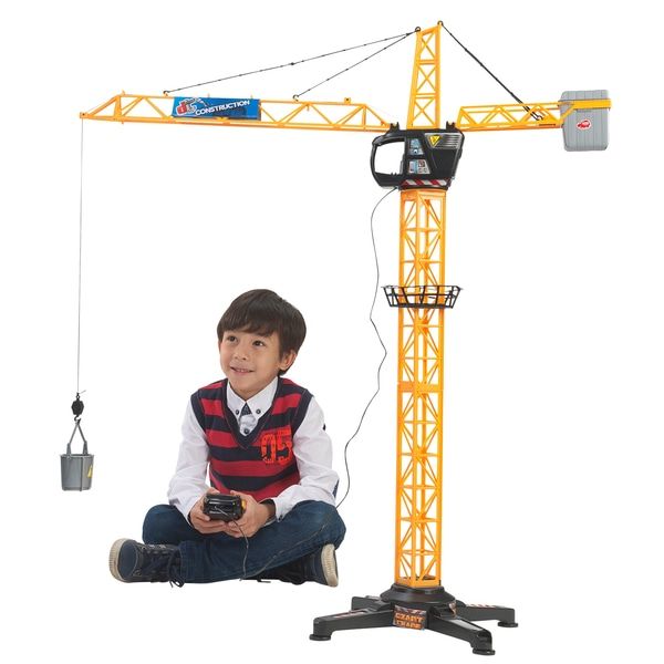 a young boy sitting on the ground in front of a construction crane holding a remote control