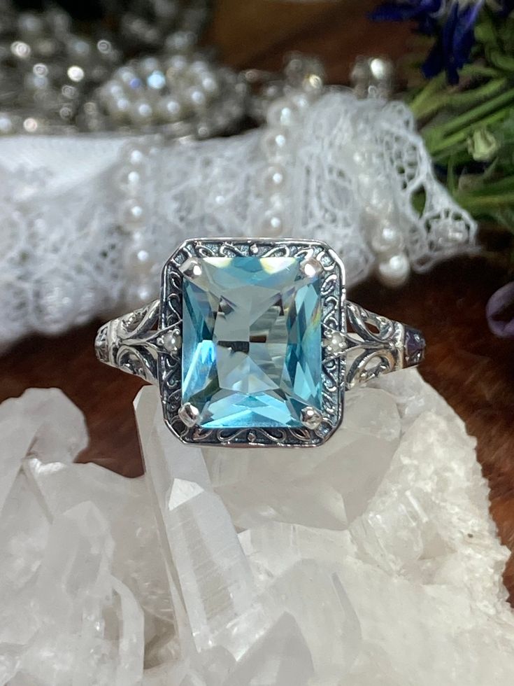 Simulated Aquamarine Ring Rectangle Seed Pearl Design#73 Custom Made Inspired by the designs of the Art Deco/Art Nouveau period; I now offer this gorgeous sterling silver reproduction ring in sterling silver. The antiqued sterling filigree setting is set with a flawless simulated aquamarine. The inside of the band is hallmarked 925 for sterling. This rectangle cut gem is 11mm (about 7/16th of an inch) long by 9mm (3/8th inch) in wide. The ring sits 7mm off the finger. Notice the beautiful Antiqu Blue Topaz Ring With Square Cut, Blue Rings With Rectangular Accent Stones, Blue Square Cut Topaz Ring, Art Deco Rectangular Ring With Accent Stones, Octagon Aquamarine Ring As A Gift, Octagon Aquamarine Ring As Gift, Octagon Aquamarine Rings For Gifts, Rectangular Silver Blue Topaz Ring, Blue Rectangular Stone Ring Fine Jewelry