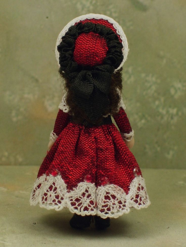 a small doll is wearing a red dress and white lace on it's head