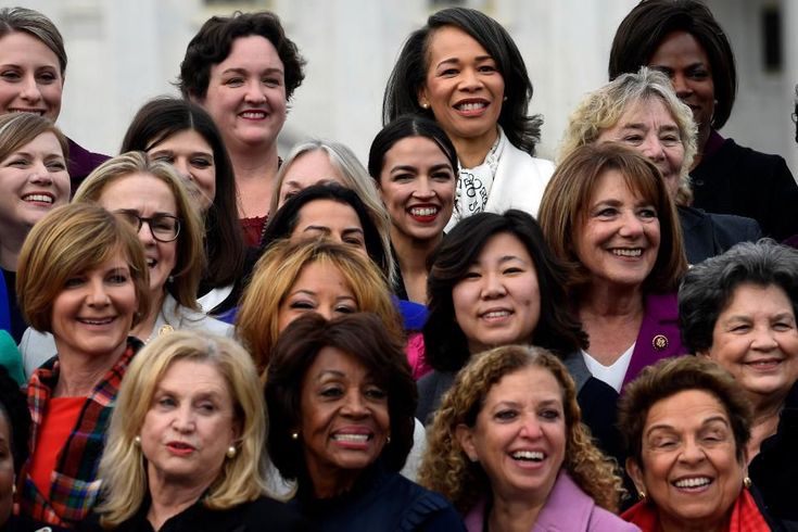 a group of women standing next to each other in front of a white building and smiling