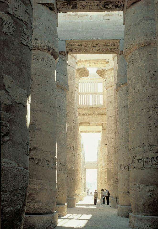 two people are standing in the middle of an ancient building with columns on either side