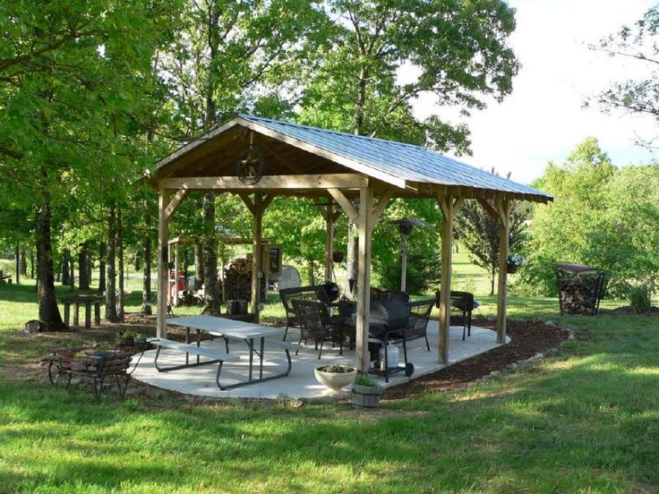 a gazebo sitting in the middle of a lush green park with picnic tables and chairs