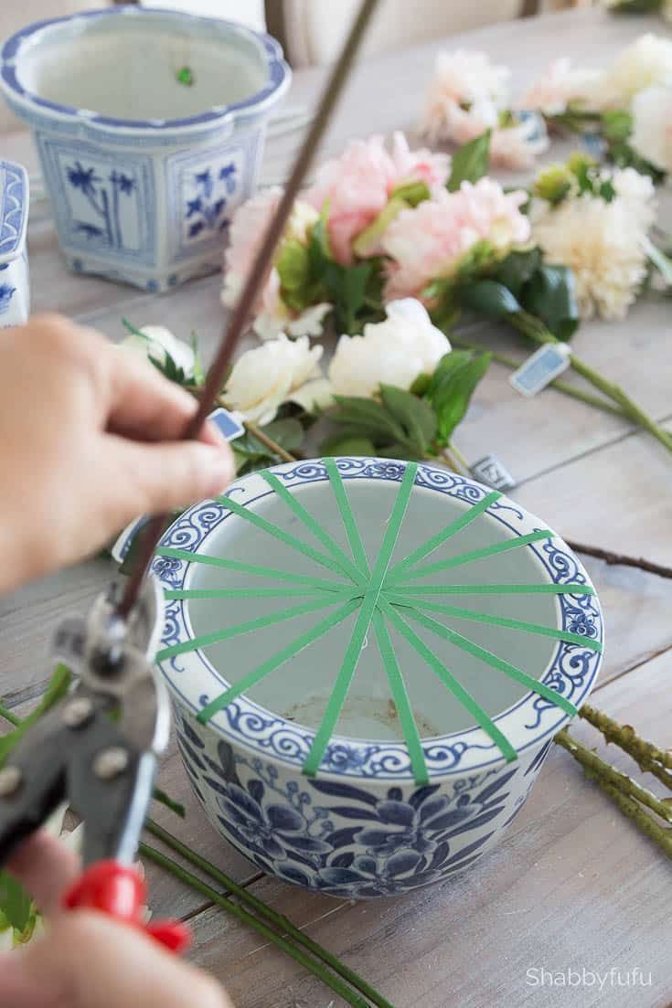 a person cutting flowers with scissors on a table next to other vases and bowls