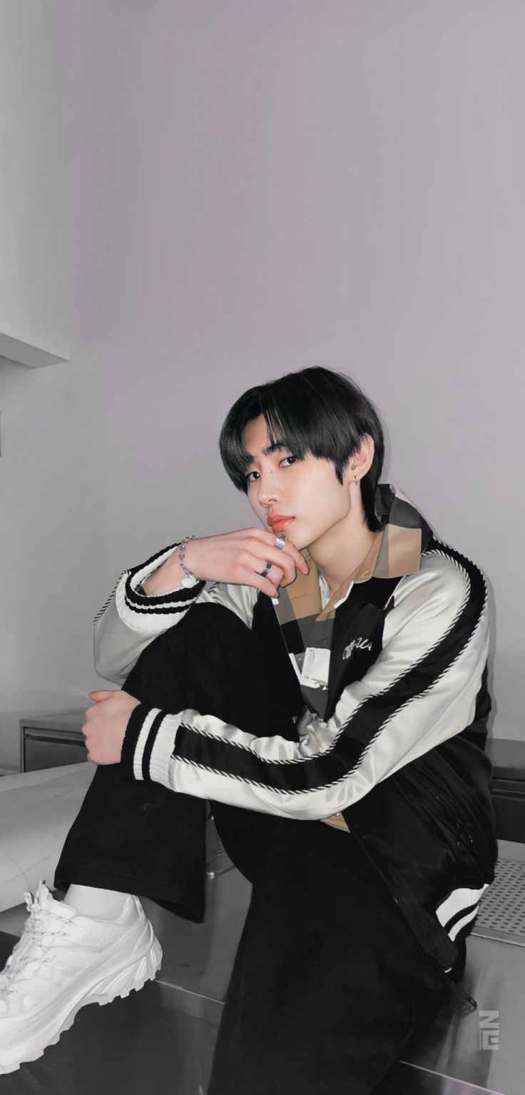 a young man sitting on top of a metal table next to a white wall and black floor