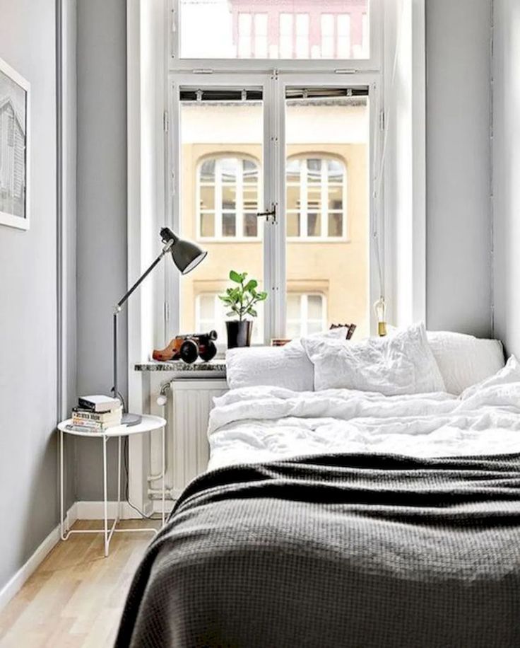 a bed sitting in a bedroom under a window next to a table with a lamp on it